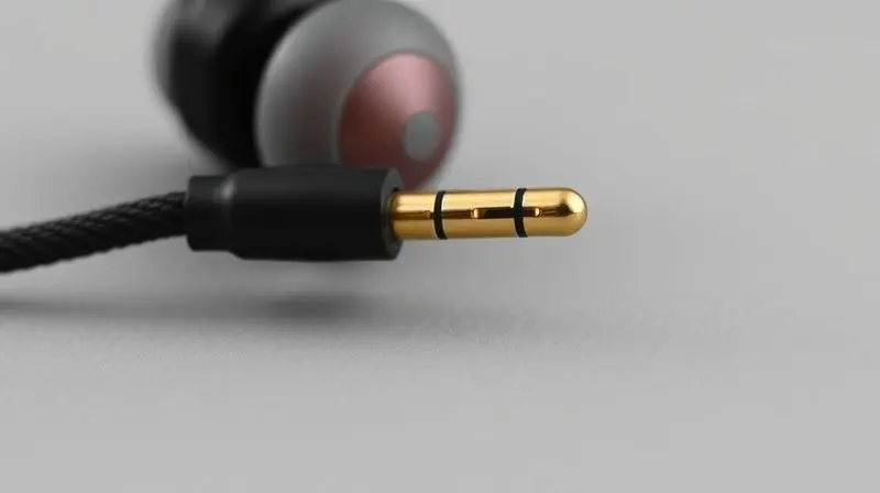 Fotografia detalhada do conector de 2 pinos de um cabo trançado sendo conectado a um fone de ouvido do tipo IEM.